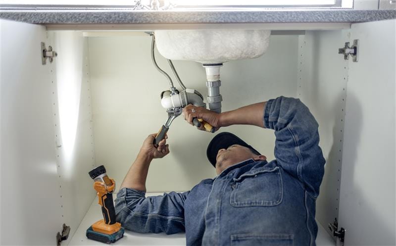 Plumber repairing pipes beneath a bathroom sink in Santa Paula